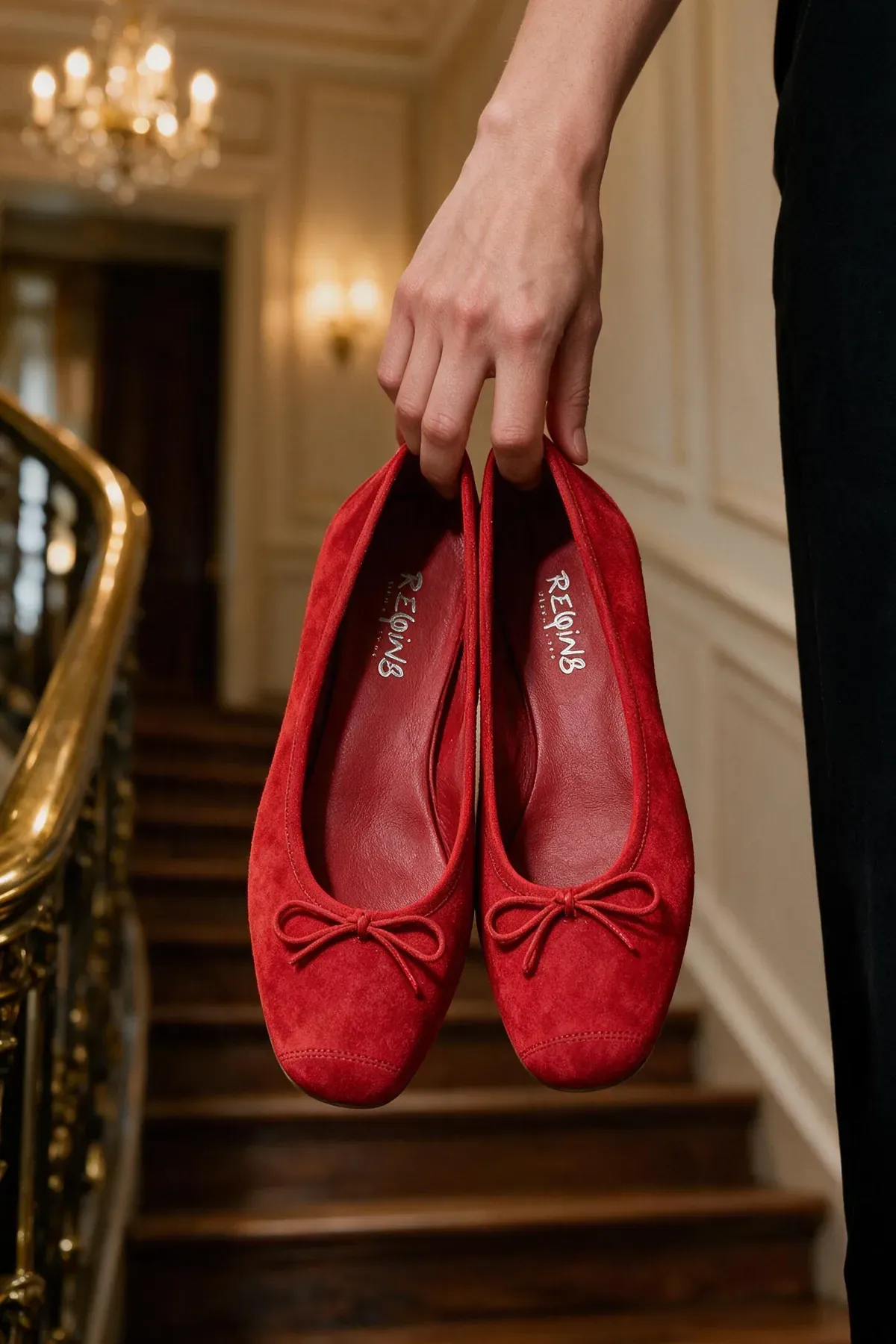 A pair of red suede ballet flats held above a Haussmann staircase.
